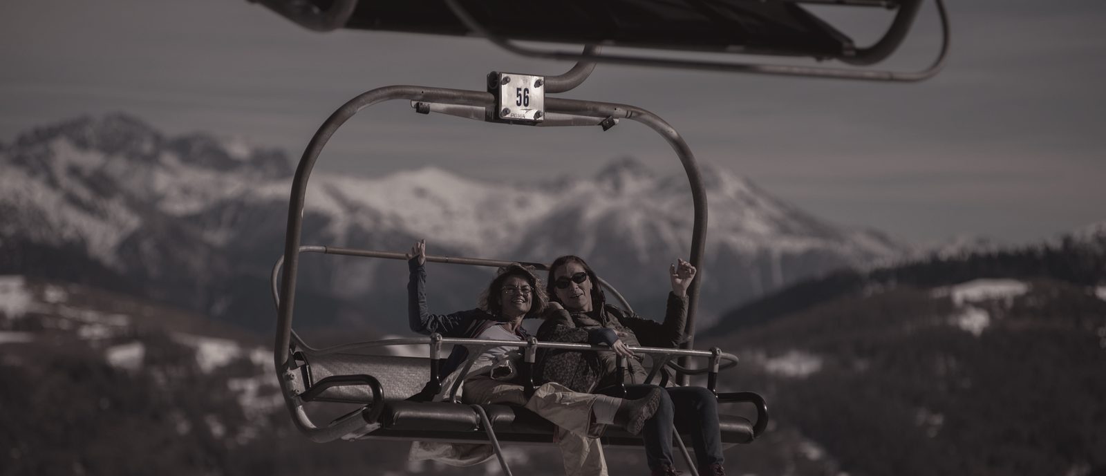 Two people riding a chairlift high above a mountain valley
