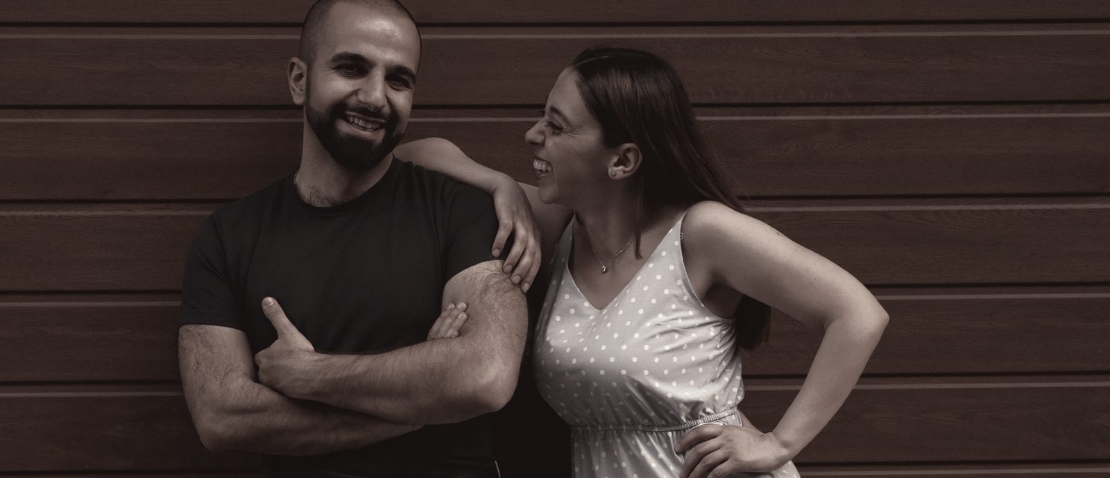 A couple laughing together against a timber wall